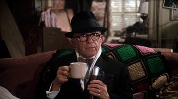 Movie still from “The Sunshine Boys” (1975), directed by Herbert Ross – An older man in a hat and glasses holding a cup of coffee; Medium shot, Over the shoulder angle
