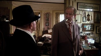 Movie still from “The Sunshine Boys” (1975), directed by Herbert Ross – A man in a suit smoking a cigarette while another man in a hat looks on; Medium shot, Over the shoulder angle