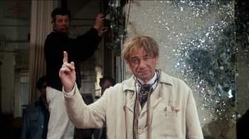 Movie still from “The Sunshine Boys” (1975), directed by Herbert Ross – An older man in a white coat is holding up his finger; Medium shot, Over the shoulder angle