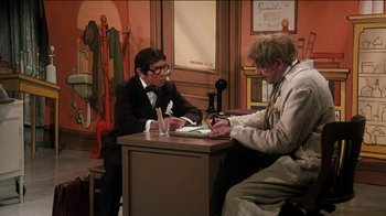 Movie still from “The Sunshine Boys” (1975), directed by Herbert Ross – Two men sitting at a desk in front of a microphone; Wide shot, High angle