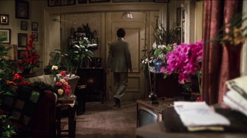 Movie still from “The Sunshine Boys” (1975), directed by Herbert Ross – A man in a suit walking through a room with flowers; Wide shot, Over the shoulder angle