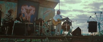 Movie still from “The Sweet Hereafter” (1997), directed by Atom Egoyan – A man with a beard is holding a guitar on a stage; Wide shot, Low angle