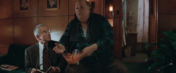 Movie still from “The Sweet Hereafter” (1997), directed by Atom Egoyan – A man sitting on a couch holding a bowl of food; Medium shot, High angle