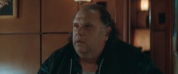 Movie still from “The Sweet Hereafter” (1997), directed by Atom Egoyan – A man with long hair and a beard is sitting in front of a door; Close Up shot, Over the shoulder angle