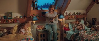 Movie still from “The Sweet Hereafter” (1997), directed by Atom Egoyan – A woman sitting on a chair reading a book in a room; Wide shot, High angle