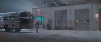 Movie still from “The Sweet Hereafter” (1997), directed by Atom Egoyan – A person holding an umbrella in front of a building; Extreme Wide shot, High angle