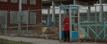 Movie still from “The Sweet Hereafter” (1997), directed by Atom Egoyan – A woman talking on the phone while standing next to a phone booth; Wide shot, High angle