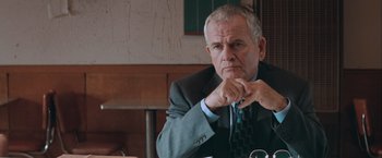 Movie still from “The Sweet Hereafter” (1997), directed by Atom Egoyan – An older man wearing a suit and tie sitting at a table; Close Up shot, Over the shoulder angle