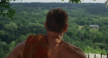 Movie still from “The Swimmer” (1968), directed by Sydney Pollack – A man sitting on top of a chair looking out over a forest; Medium shot, High angle