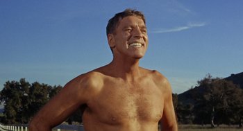 Movie still from “The Swimmer” (1968), directed by Sydney Pollack – A man with no shirt is smiling for the camera; Medium shot, Low angle