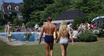 Movie still from “The Swimmer” (1968), directed by Sydney Pollack – A man and a woman holding hands near a swimming pool; Wide shot, High angle