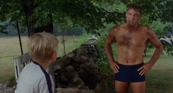 Movie still from “The Swimmer” (1968), directed by Sydney Pollack – A man in blue trunks standing next to a young boy; Medium shot, Over the shoulder angle