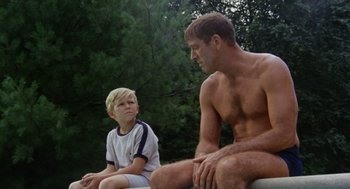 Movie still from “The Swimmer” (1968), directed by Sydney Pollack – A man sitting next to a young boy in a park; Medium shot, Over the shoulder angle