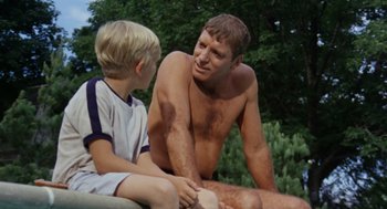 Movie still from “The Swimmer” (1968), directed by Sydney Pollack – A man sitting next to a young boy in the grass; Medium shot, Over the shoulder angle