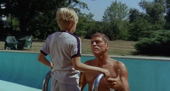 Movie still from “The Swimmer” (1968), directed by Sydney Pollack – A man and a boy standing next to each other near a swimming pool; Medium shot, Low angle