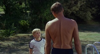 Movie still from “The Swimmer” (1968), directed by Sydney Pollack – A man and a boy standing next to each other in the grass; Medium shot, Over the shoulder angle