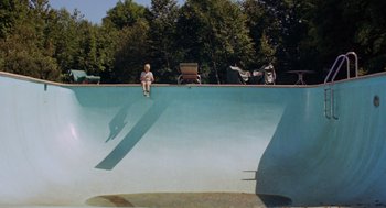 Movie still from “The Swimmer” (1968), directed by Sydney Pollack – A man sitting on the edge of a swimming pool; Extreme Wide shot, Overhead angle