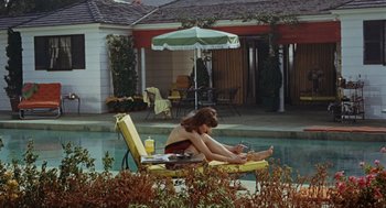 Movie still from “The Swimmer” (1968), directed by Sydney Pollack – A woman sitting on a lawn chair next to a swimming pool; Wide shot, High angle