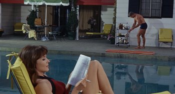 Movie still from “The Swimmer” (1968), directed by Sydney Pollack – A woman sitting on the side of a pool reading a book; Wide shot, High angle