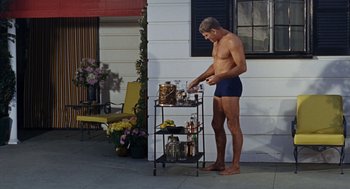 Movie still from “The Swimmer” (1968), directed by Sydney Pollack – A man in his underwear is standing next to a cart of drinks on a porch; Medium shot, Low angle