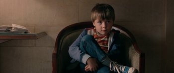 Movie still from “The Switch” (2010), directed by Josh Gordon – A young boy sitting in a chair with his legs crossed; Close Up shot, High angle