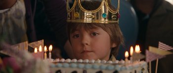 Movie still from “The Switch” (2010), directed by Josh Gordon – A young boy wearing a crown sitting in front of a birthday cake; Close Up shot, Over the shoulder angle
