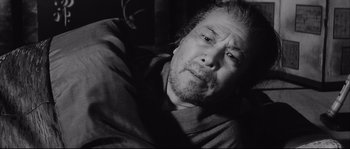 Movie still from “The Sword of Doom” (1966), directed by Kihachi Okamoto – An older man with a beard and mustache is laying on a couch; Close Up shot, Low angle