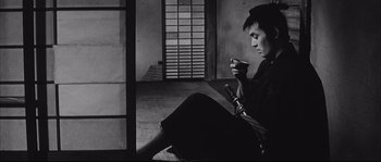 Movie still from “The Sword of Doom” (1966), directed by Kihachi Okamoto – A man sitting on the ground holding a cup; Medium shot, Low angle