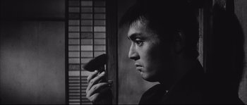 Movie still from “The Sword of Doom” (1966), directed by Kihachi Okamoto – A black and white photo of a man holding a cell phone; Close Up shot, Low angle