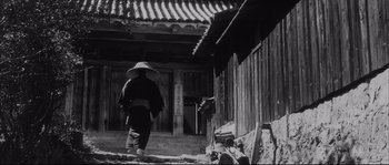 Movie still from “The Sword of Doom” (1966), directed by Kihachi Okamoto – A man wearing a hat walking down a street; Wide shot, Low angle