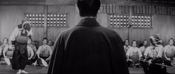Movie still from “The Sword of Doom” (1966), directed by Kihachi Okamoto – A man standing in front of a group of people; Medium shot, Over the shoulder angle