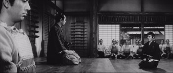 Movie still from “The Sword of Doom” (1966), directed by Kihachi Okamoto – A man sitting on the ground in front of a group of people; Wide shot, Over the shoulder angle