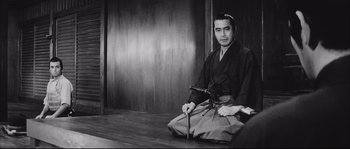 Movie still from “The Sword of Doom” (1966), directed by Kihachi Okamoto – A man sitting on the ground holding a sword; Medium shot, Over the shoulder angle