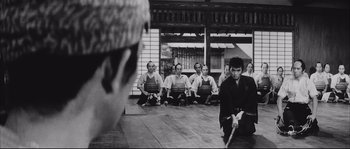 Movie still from “The Sword of Doom” (1966), directed by Kihachi Okamoto – A group of men sitting on the ground watching a man with a sword in his hands; Wide shot, High angle