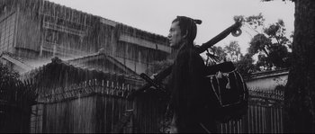 Movie still from “The Sword of Doom” (1966), directed by Kihachi Okamoto – A man standing in the pouring rain holding two swords; Medium shot, Low angle