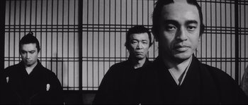 Movie still from “The Sword of Doom” (1966), directed by Kihachi Okamoto – Two men standing next to each other in front of a fence; Close Up shot, Low angle