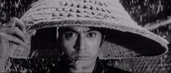 Movie still from “The Sword of Doom” (1966), directed by Kihachi Okamoto – A man wearing a straw hat with a cigarette sticking out of his mouth; Close Up shot, Low angle