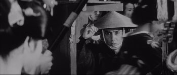 Movie still from “The Sword of Doom” (1966), directed by Kihachi Okamoto – A man wearing a conical hat is standing next to another man; Close Up shot, Low angle
