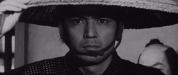 Movie still from “The Sword of Doom” (1966), directed by Kihachi Okamoto – A man wearing a straw hat and a black shirt; Close Up shot, Low angle