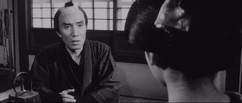 Movie still from “The Sword of Doom” (1966), directed by Kihachi Okamoto – A black and white photo of a man talking to another man; Close Up shot, Over the shoulder angle
