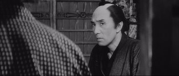 Movie still from “The Sword of Doom” (1966), directed by Kihachi Okamoto – A man with a shaved head looks at the camera; Close Up shot, Over the shoulder angle