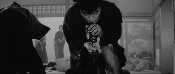 Movie still from “The Sword of Doom” (1966), directed by Kihachi Okamoto – A man holding a sword while standing next to another man; Medium shot, Over the shoulder angle