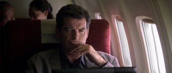 Movie still from “The Tailor of Panama” (2001), directed by John Boorman – A man sitting on a seat on an airplane looking at a computer screen; Close Up shot, Over the shoulder angle