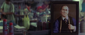 Movie still from “The Tailor of Panama” (2001), directed by John Boorman – A picture of a person in a room with people in the background; Extreme Close Up shot, Over the shoulder angle