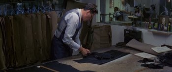 Movie still from “The Tailor of Panama” (2001), directed by John Boorman – A man cutting fabric on a table in a room; Medium shot, High angle