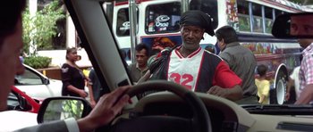 Movie still from “The Tailor of Panama” (2001), directed by John Boorman – A man with a black hat is riding a bus; Medium shot, Over the shoulder angle