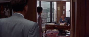 Movie still from “The Tailor of Panama” (2001), directed by John Boorman – A man sitting at a desk in front of a woman; Wide shot, Over the shoulder angle