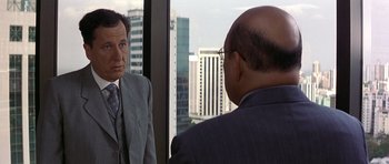 Movie still from “The Tailor of Panama” (2001), directed by John Boorman – A man looking at himself in the mirror in front of another man; Medium shot, Over the shoulder angle