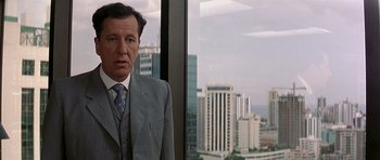 Movie still from “The Tailor of Panama” (2001), directed by John Boorman – A man standing in front of a window with a city view; Close Up shot, Over the shoulder angle