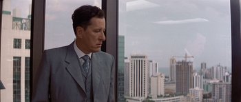Movie still from “The Tailor of Panama” (2001), directed by John Boorman – A man in a suit looking out of a window; Medium shot, Low angle